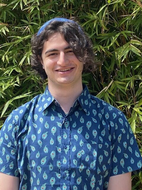 A portrait of David from the chest up, smiling and wearing a bandana and a button down shirt